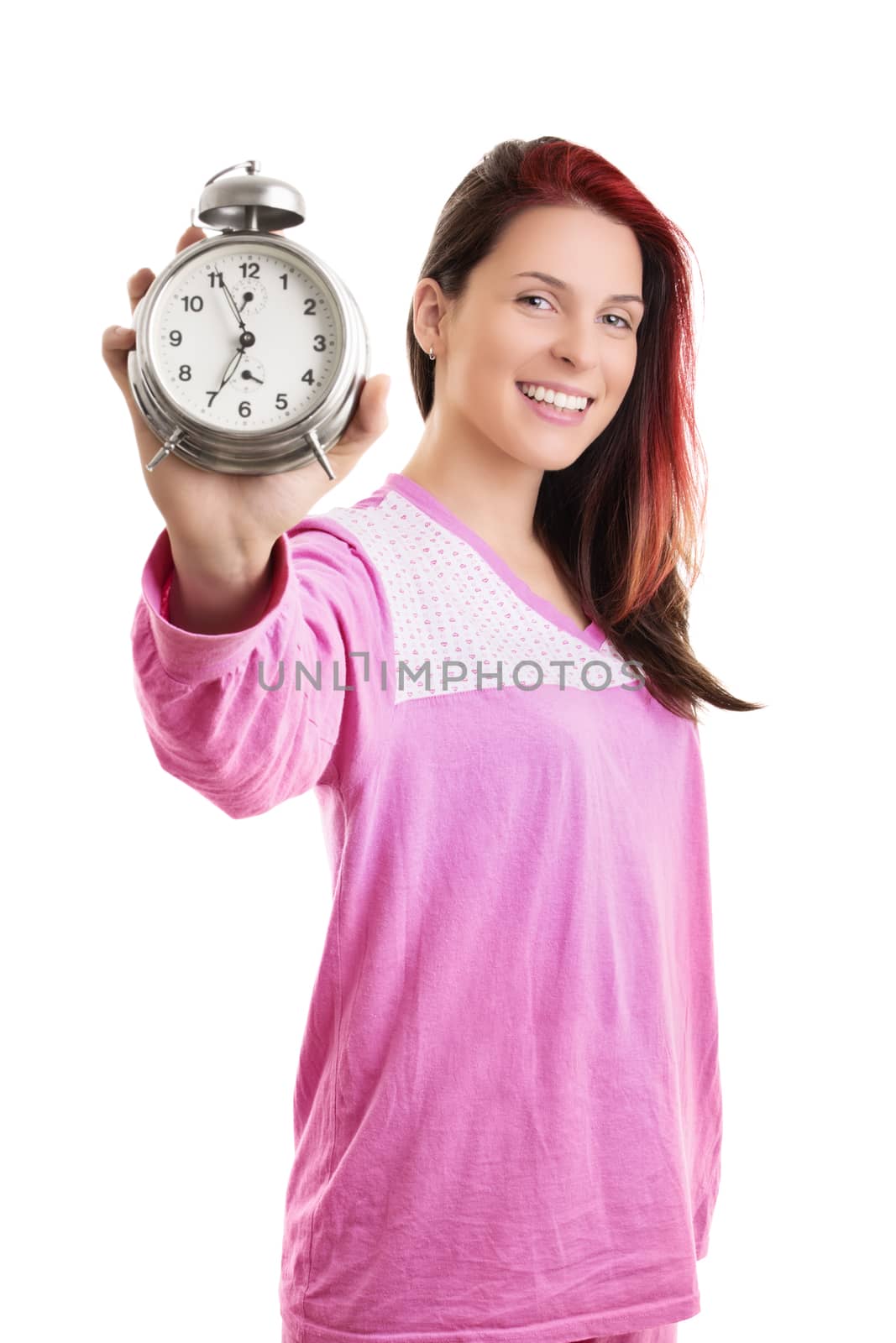 Early morning concept. Beautiful young woman in pink pajamas smiling widely and holding an old fashioned alarm clock, isolated on white background.