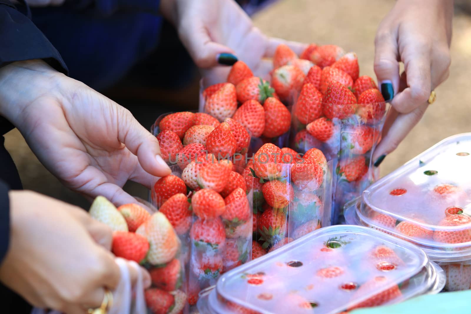 Woman hand buys strawberry from seller,Strawberry in plastic packaging for sell. Focus on hand