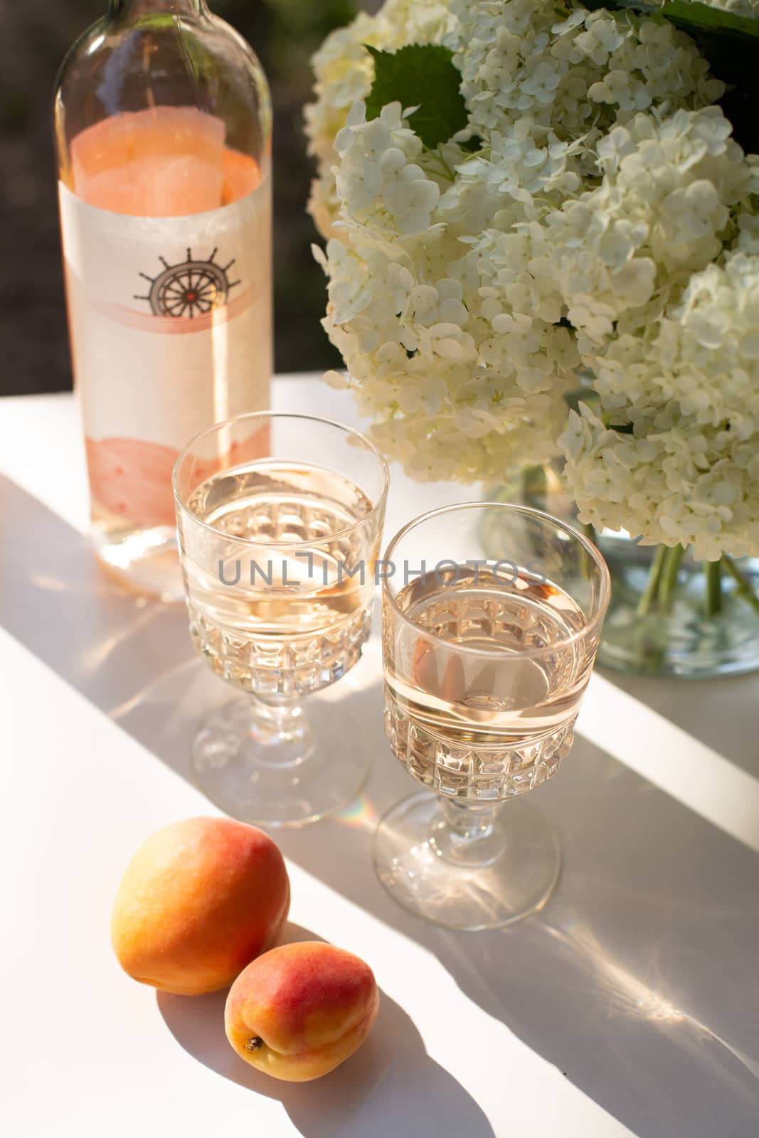 Rose wine in glasses. Rose wine on golden bottles background with flowers and fruits