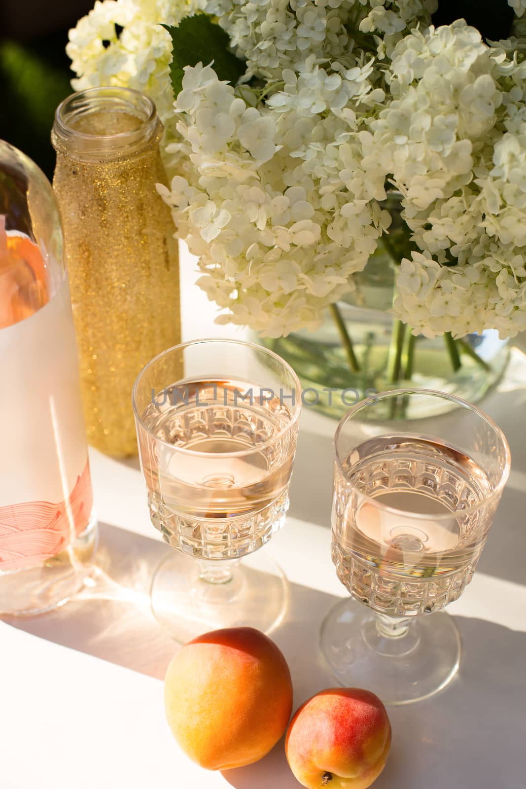 Rose wine in glasses. Rose wine on golden bottles background with flowers and fruits