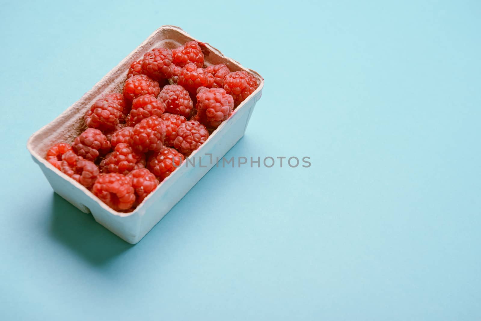 box of fresh raspberries on a blue background