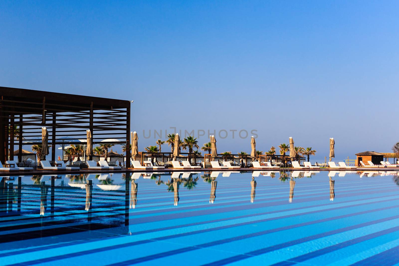 pool with wooden banks in the morning with palm trees on the beach umbrellas stacked sun beds empty without people