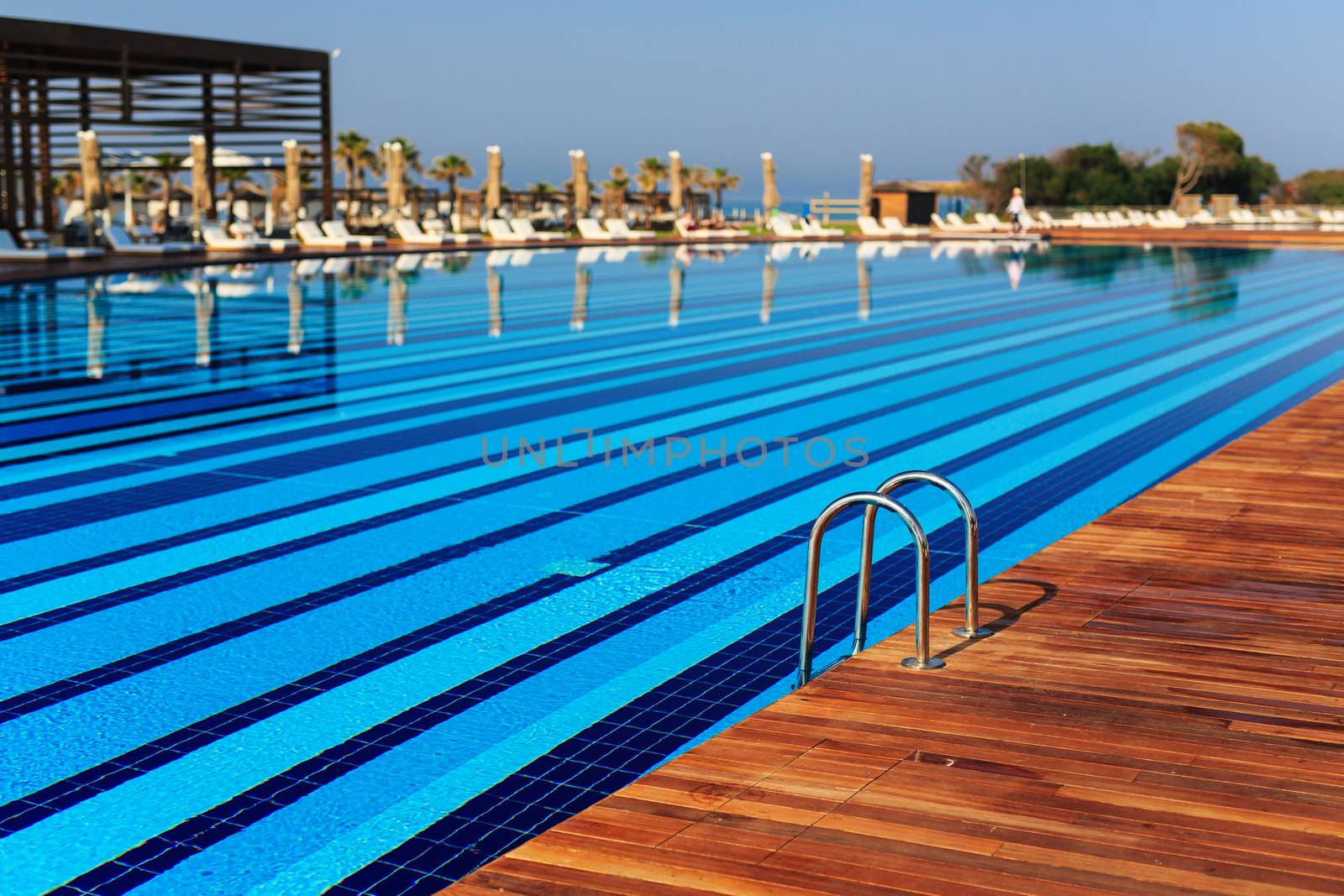 pool with wooden banks in the morning with palm trees on the beach umbrellas stacked sun beds empty without people by dikkens