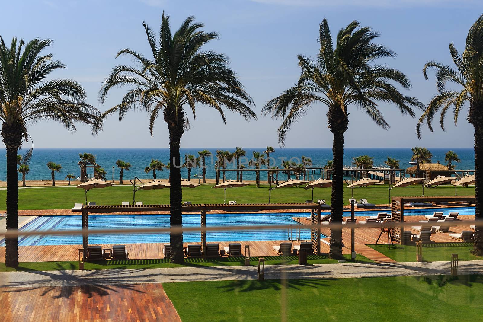 hotel grounds with swimming pool, clear blue sea and trees, summer Sunny day palm trees and sand