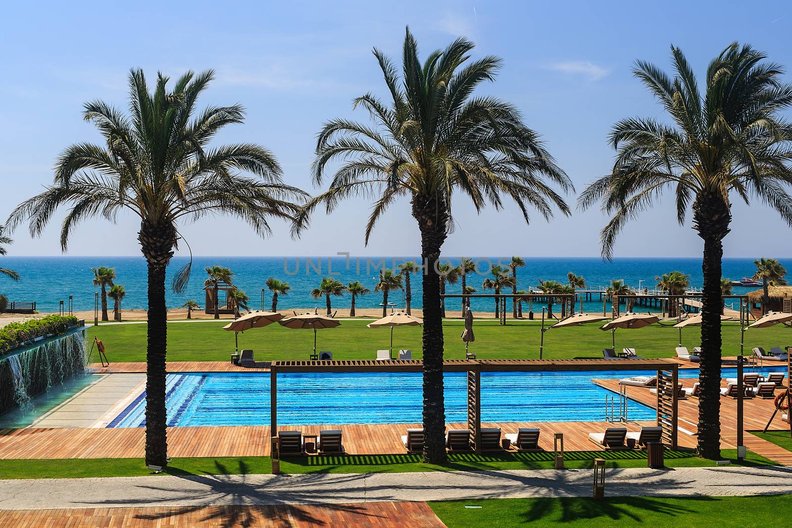 hotel grounds with swimming pool, clear blue sea and trees, summer Sunny day palm trees and sand