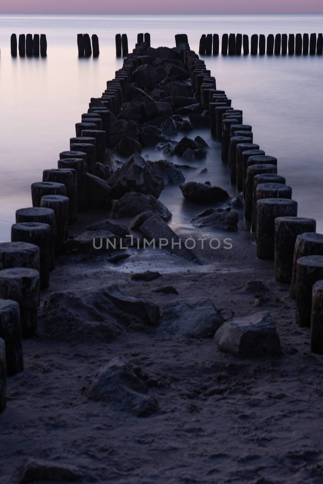 A photograph of wooden breakwater and seagulls at sunset on the Baltic Sea