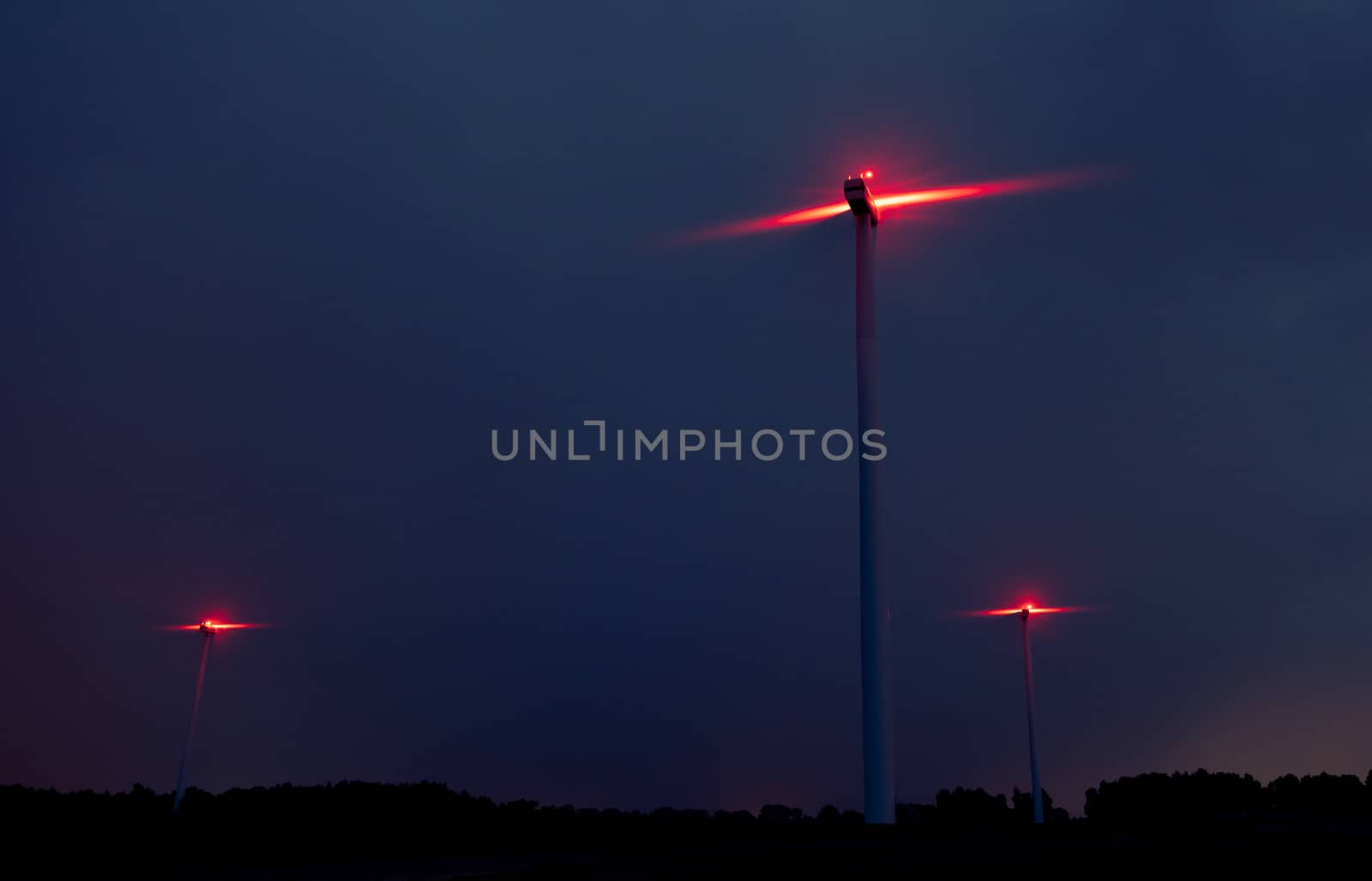 Wind turbines on a dramatic dark blue clouds in the sky. Storm ahead is coming. Red warning light on the windmill