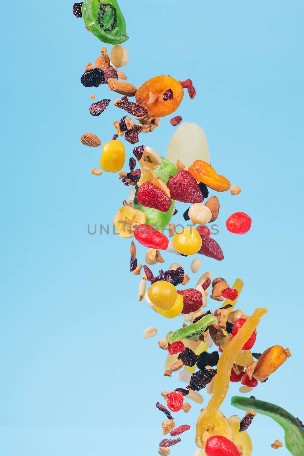 Dried and candied fruits and nuts flying on blue background. Stock photo of healty and nutrient food. Conceptual photo of vegan and vegetarian healty food.