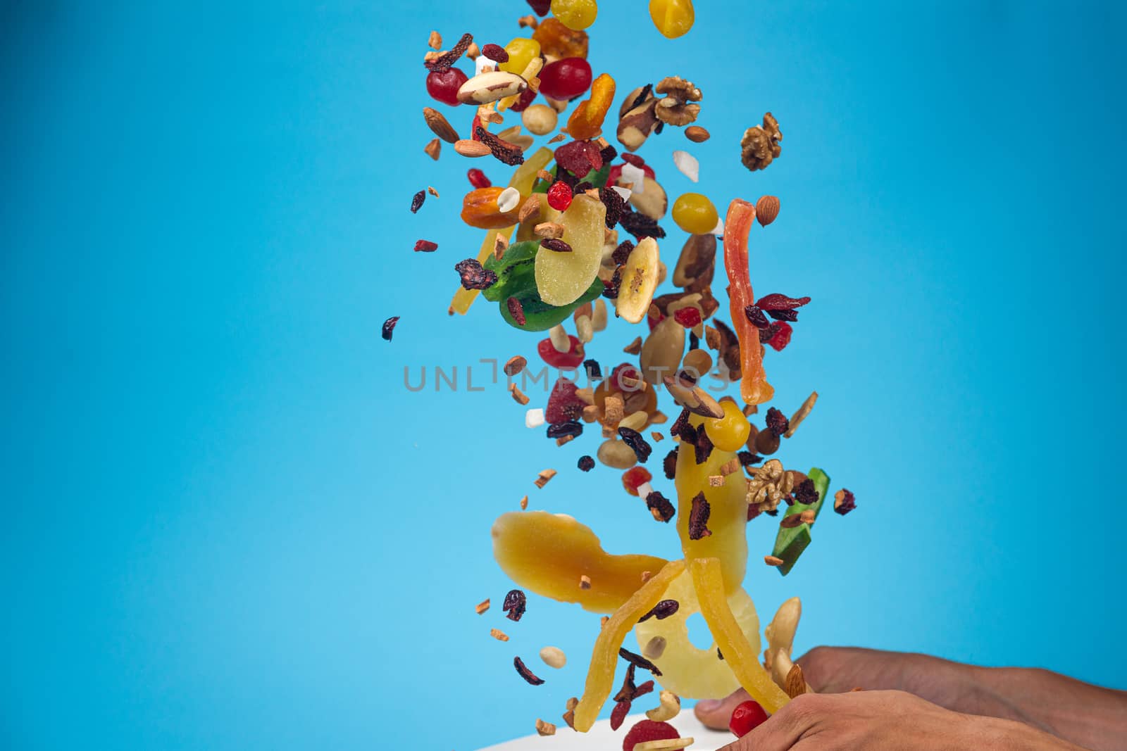 Male hands holding an empty white bowl on blue background. Candied fruits and nuts flying above the bowl. Stock photo of nutrient and healty food. Conceptual photo of vegan and vegetarial food and meal.