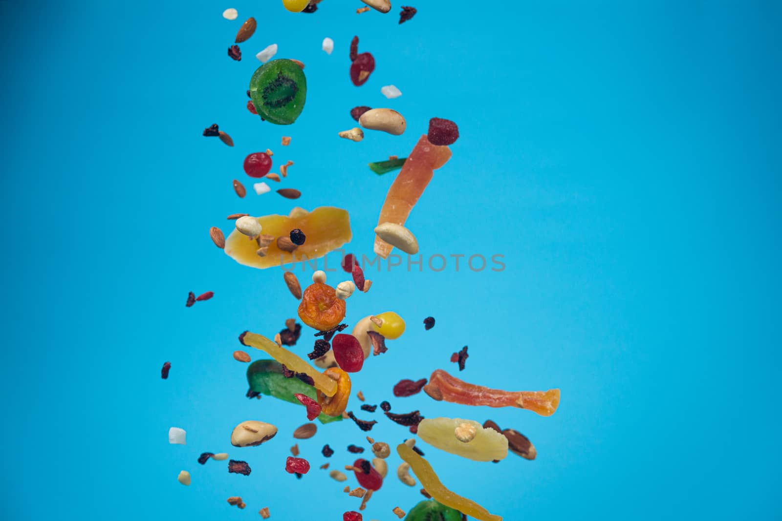 Dried and candied fruits and nuts flying on blue background. Stock photo of healty and nutrient food. Conceptual photo of vegan and vegetarian healty food.