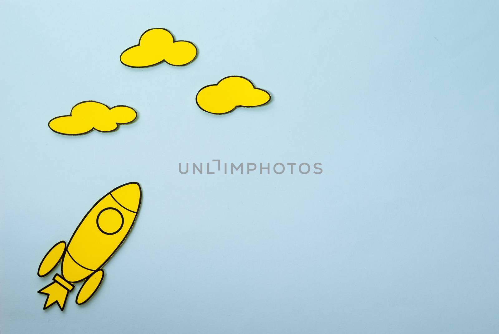 Little yellow rocket flying high aiming for the clouds in a concept of ambition and success over a blue background with copy space