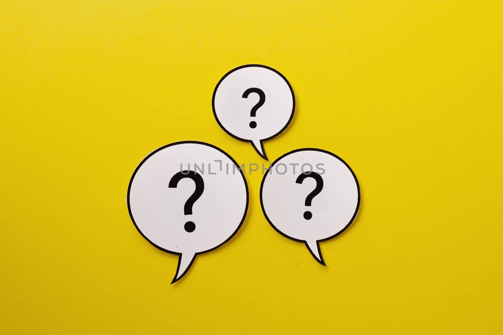 Three speech bubbles with question marks centered over a bright yellow background with copy space