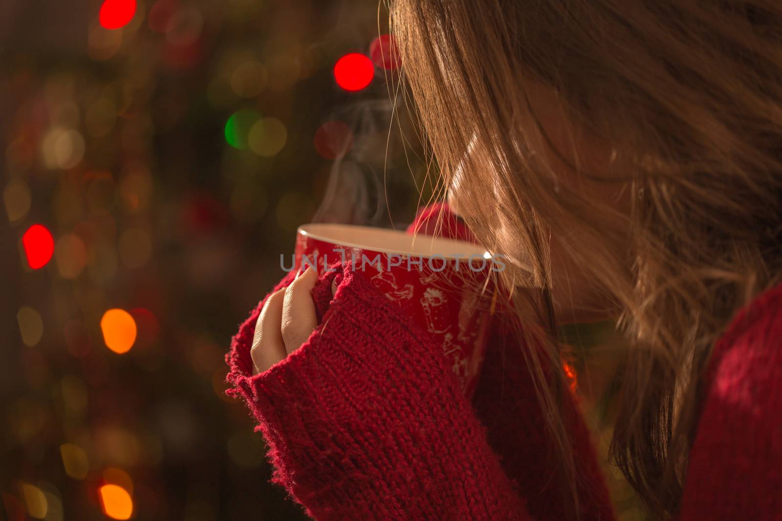 Young woman with cup of hot chocolate or tea or coffee in front of Christmas tree