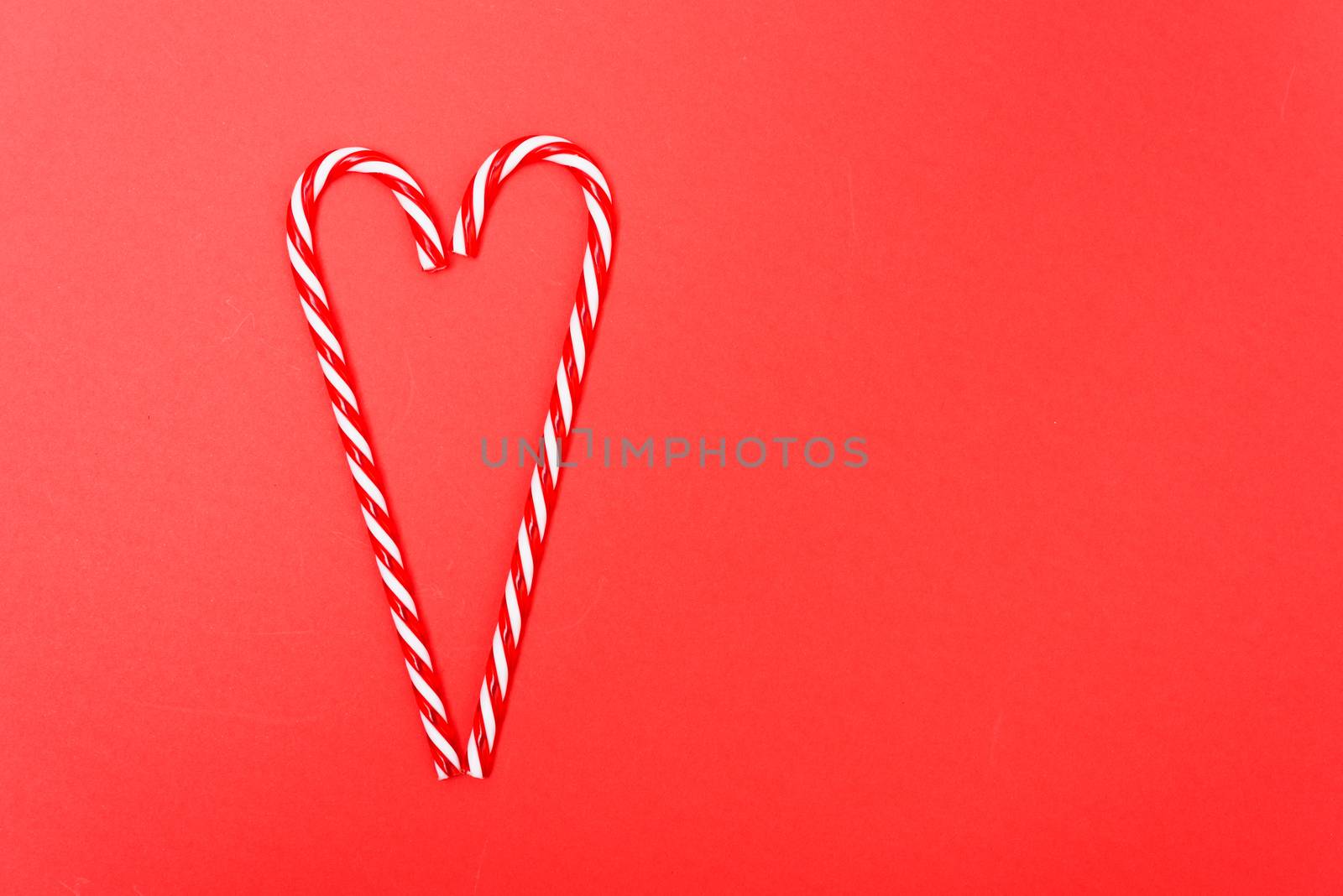 Two candy canes made making Heart of Christmas candies on red background with copy space