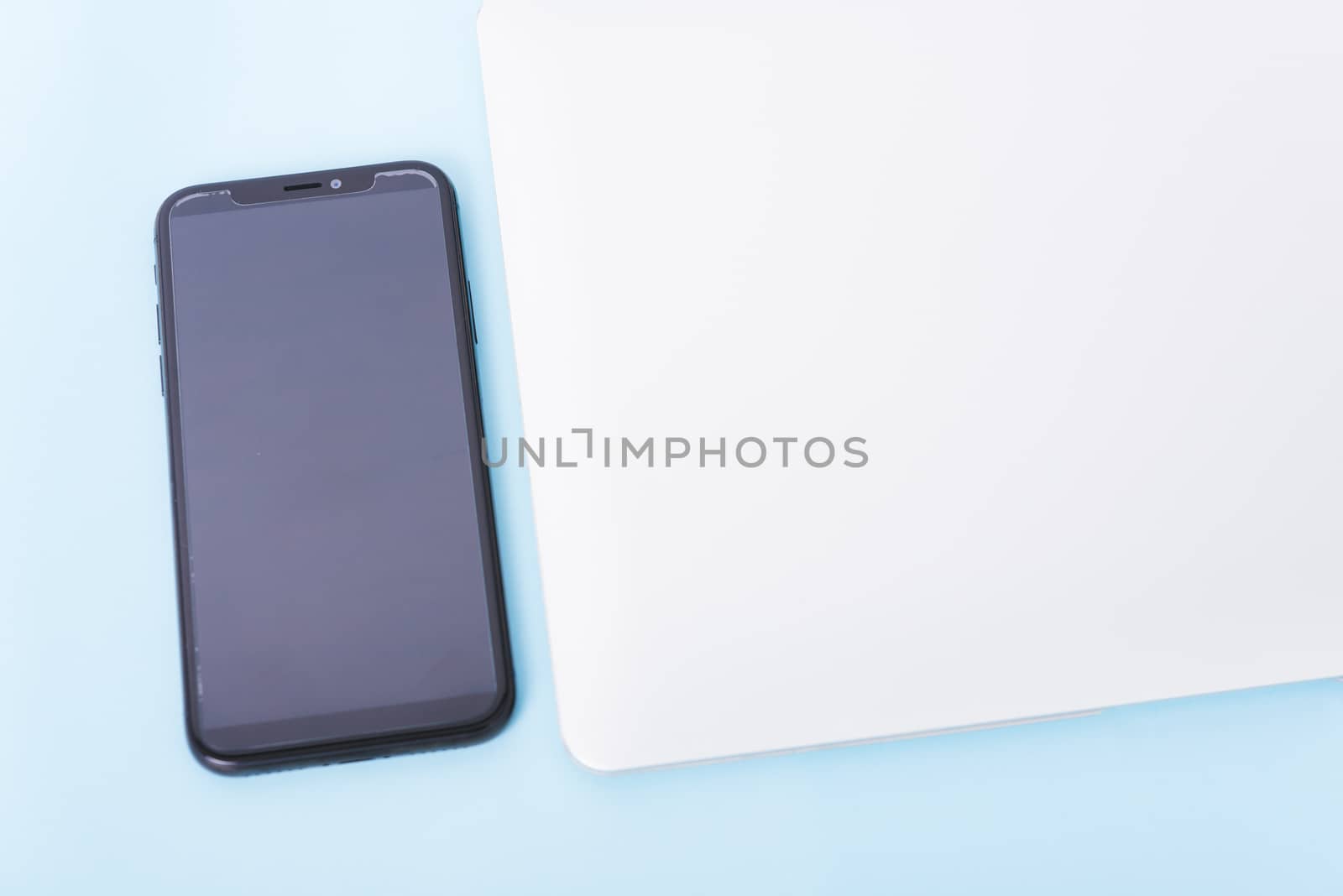 Top view close cover laptop computer notebook, smart phone and wireless mouse isolated on blue background