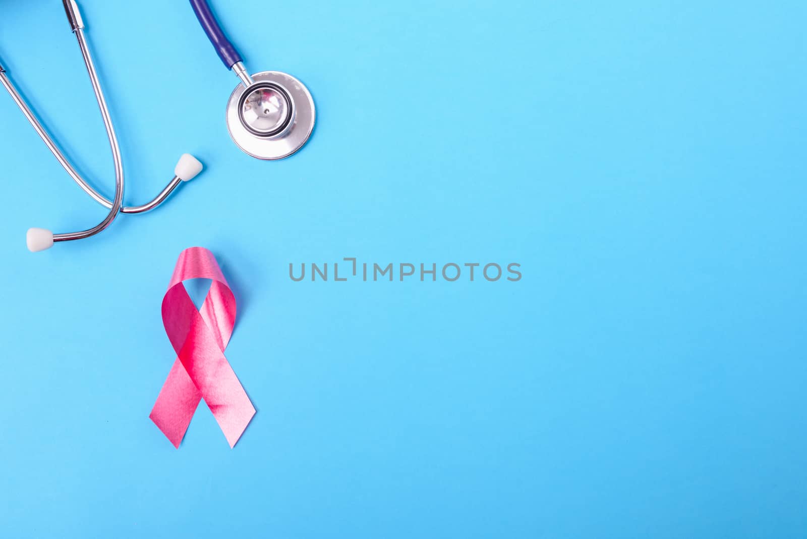 Breast cancer month concept, flat lay top view, pink ribbon and stethoscope on blue background with copy space for your text