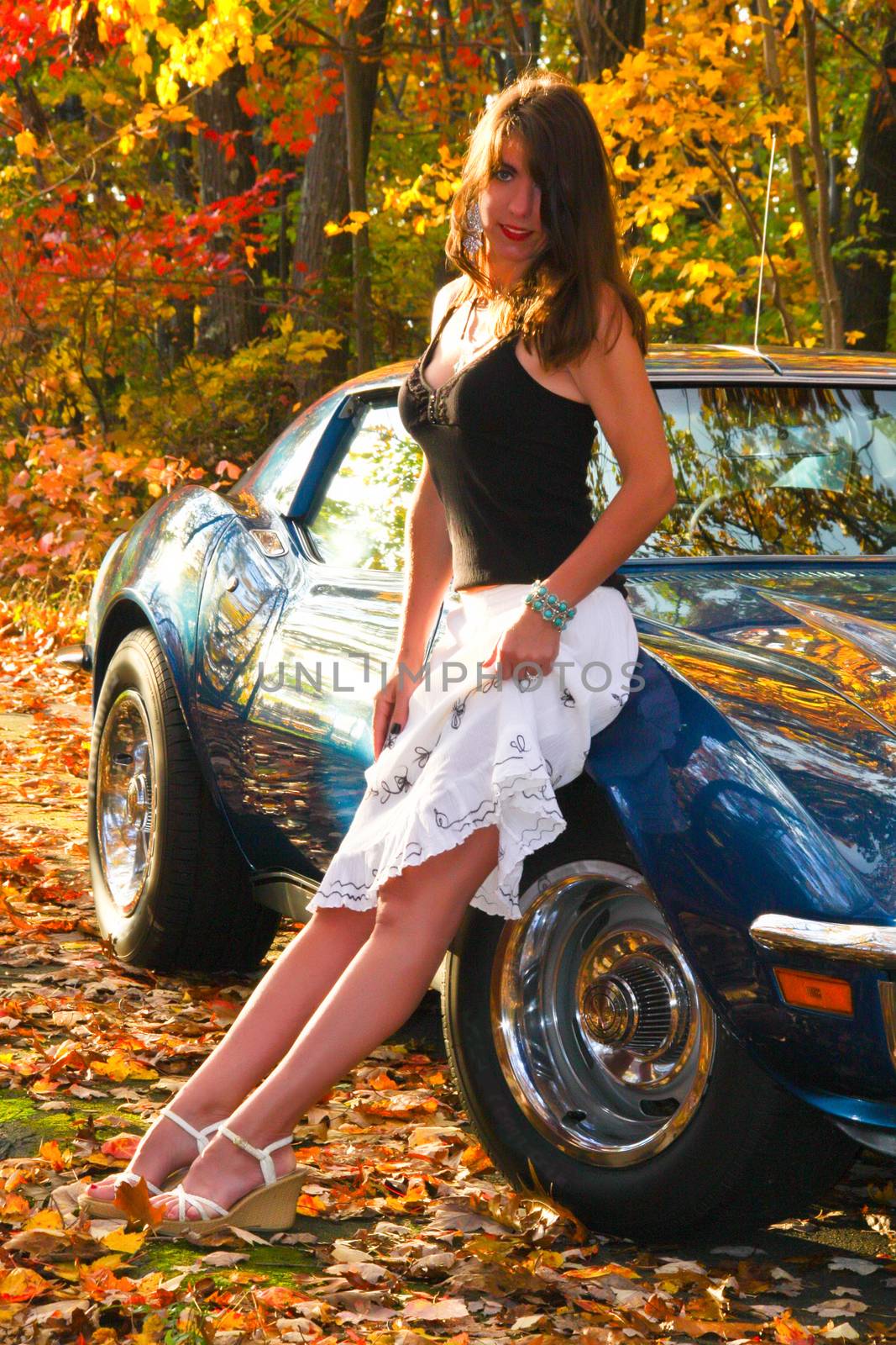 Pretty girl in dress leaning on car in fall leaves and foliage