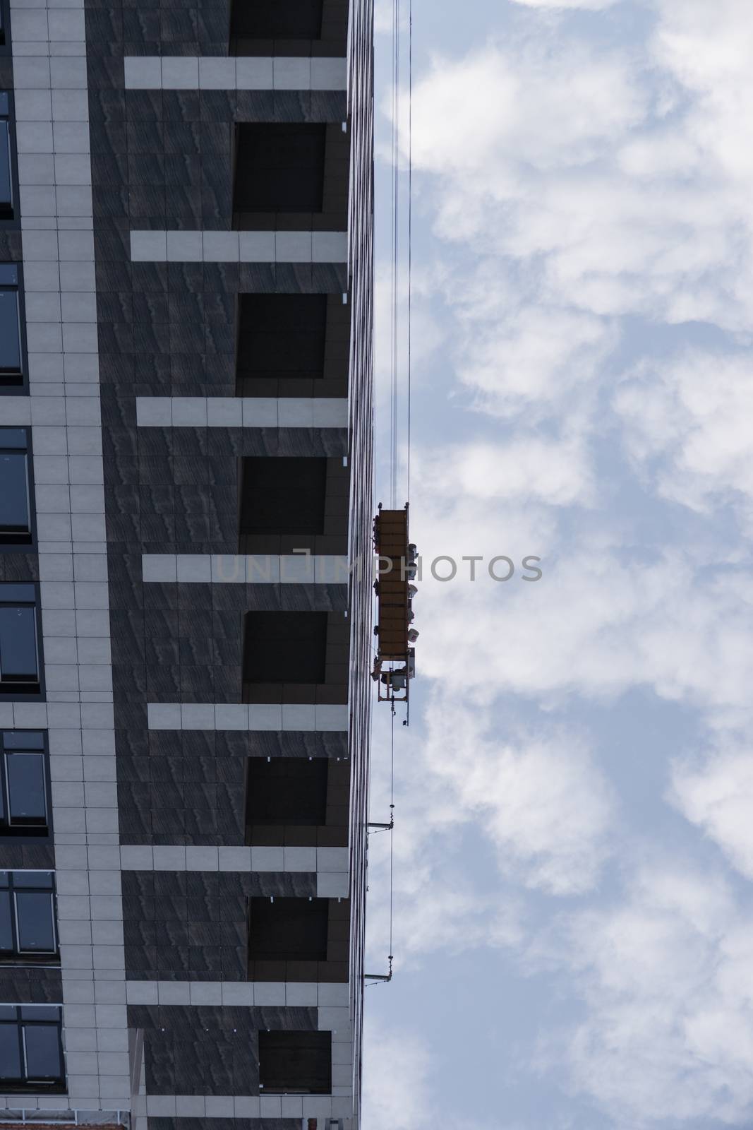 Conceptual inverted photo of workers in a cradle near a modern high-rise building