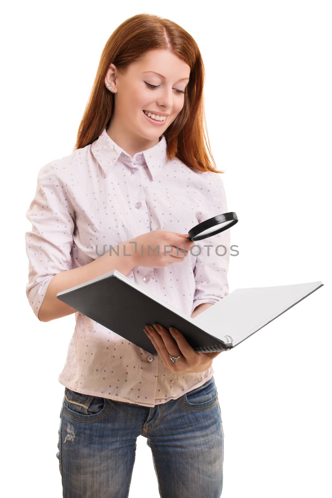 Research concept. Portrait of a beautiful smiling female in smart casual clothes, looking through a magnifying glass at an open book, isolated on white background.