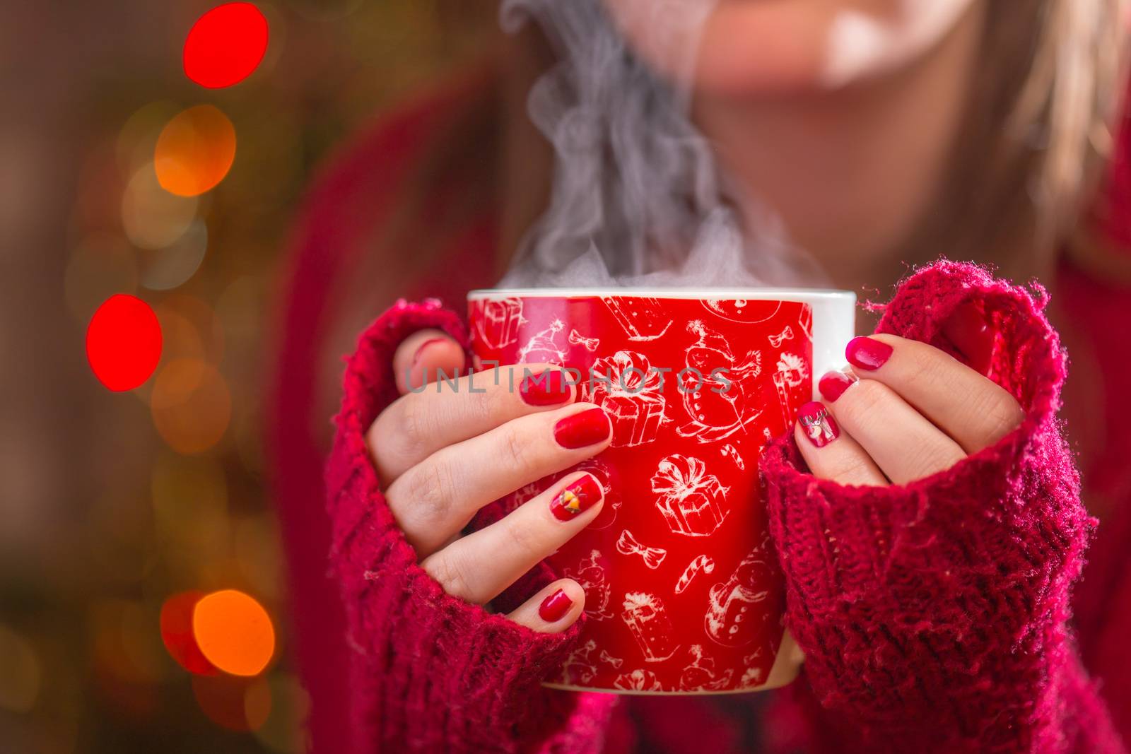 Detail of woman hands holding warm a cup of tea with steam. Blur Christmas background.