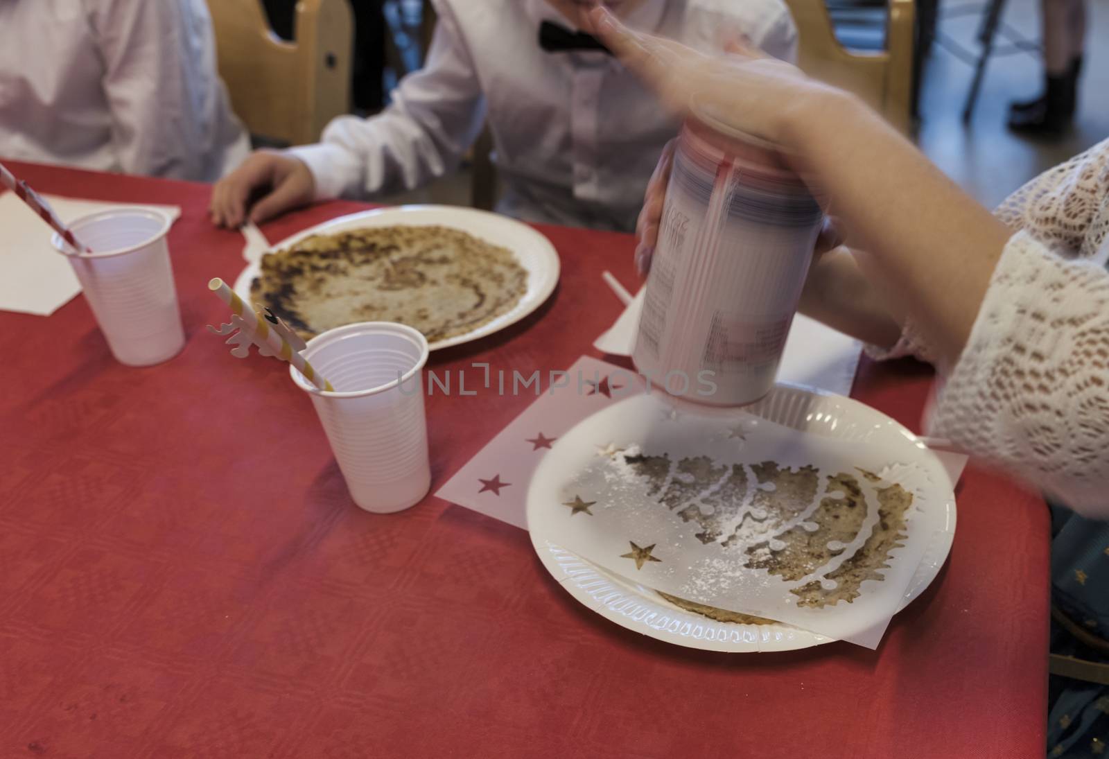 children at the table busy sprinkling pancakes with powdered sugar for the Christmas meal