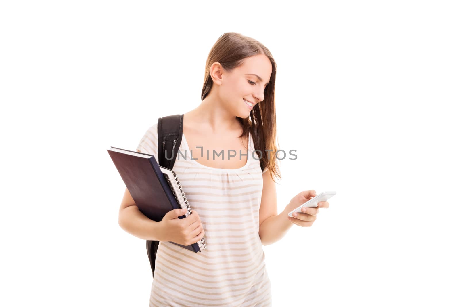 Beautiful young student girl with a backpack, holding notebooks, smiling and looking at her phone, isolated on white background.
