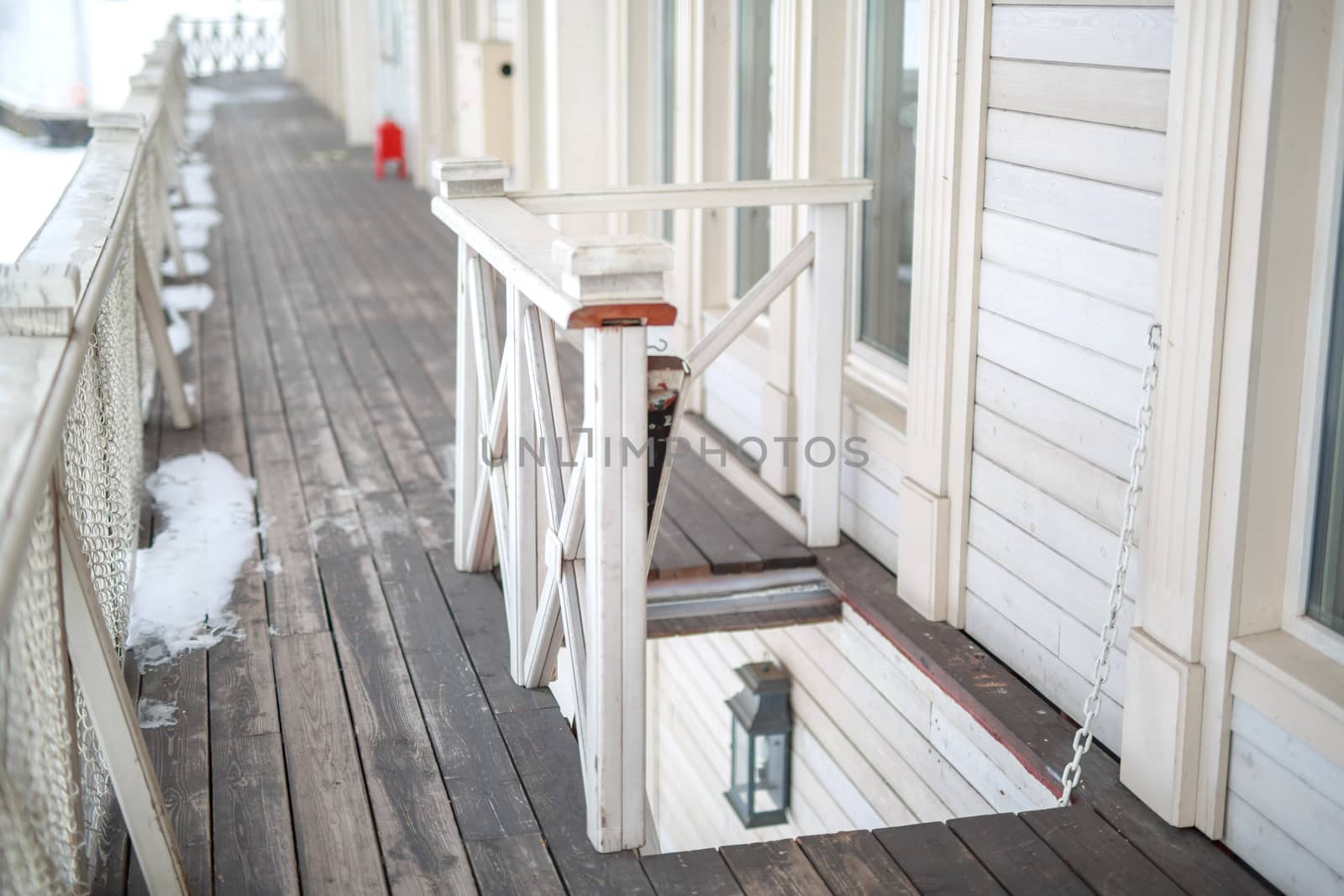 white snow on the wooden vintage open deck, old peeling paint light milk color, steel and copper lanterns hanging on the wall, snowy winter, snow lies on the river and the far shore of the earth is vi