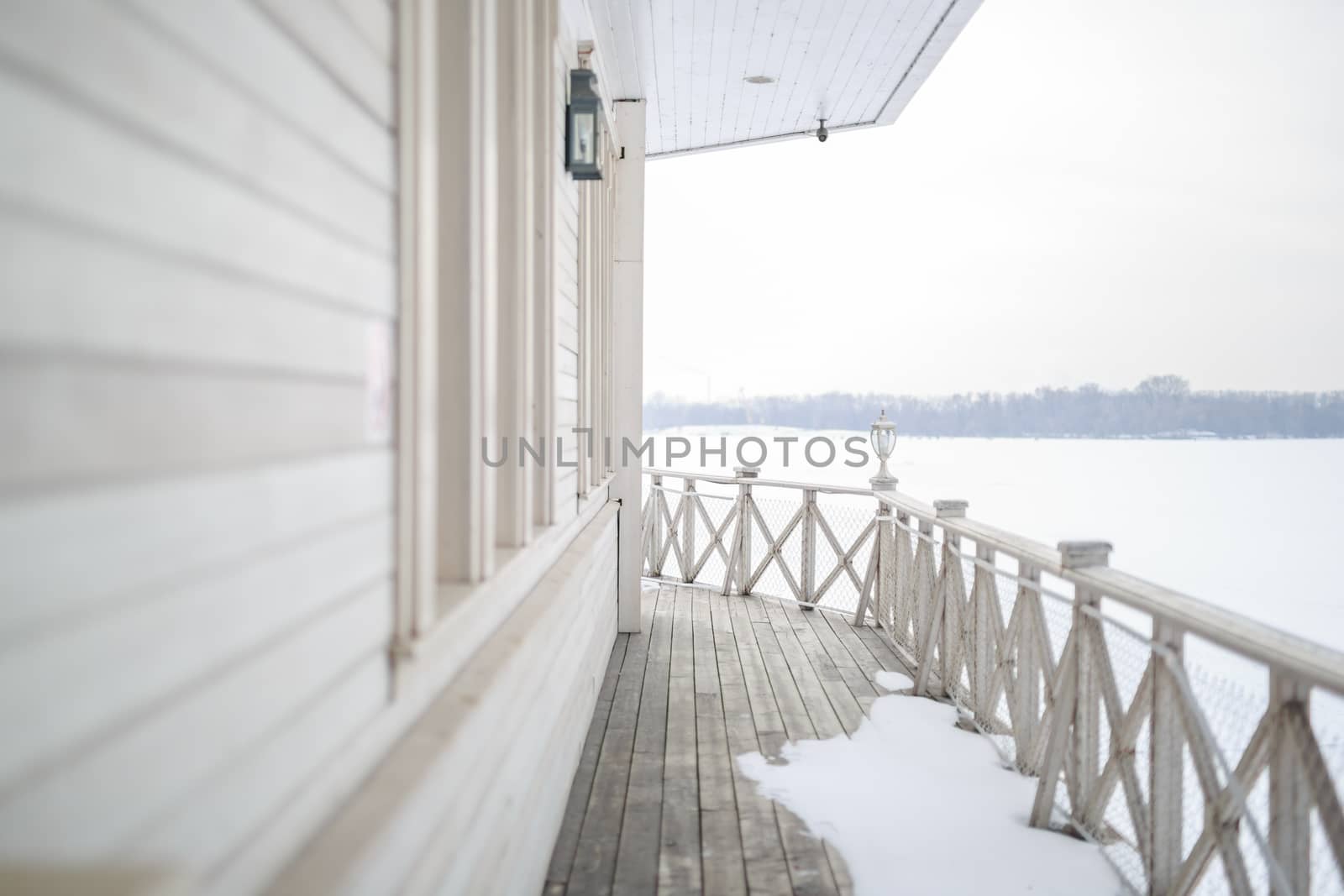 white snow on the wooden vintage open deck, old peeling paint light milk color, steel and copper lanterns hanging on the wall, snowy winter, snow lies on the river and the far shore of the earth is vi by dikkens