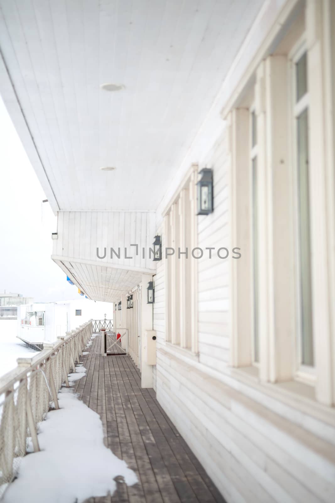 white snow on the wooden vintage open deck, old peeling paint light milk color, steel and copper lanterns hanging on the wall, snowy winter, snow lies on the river and the far shore of the earth is vi