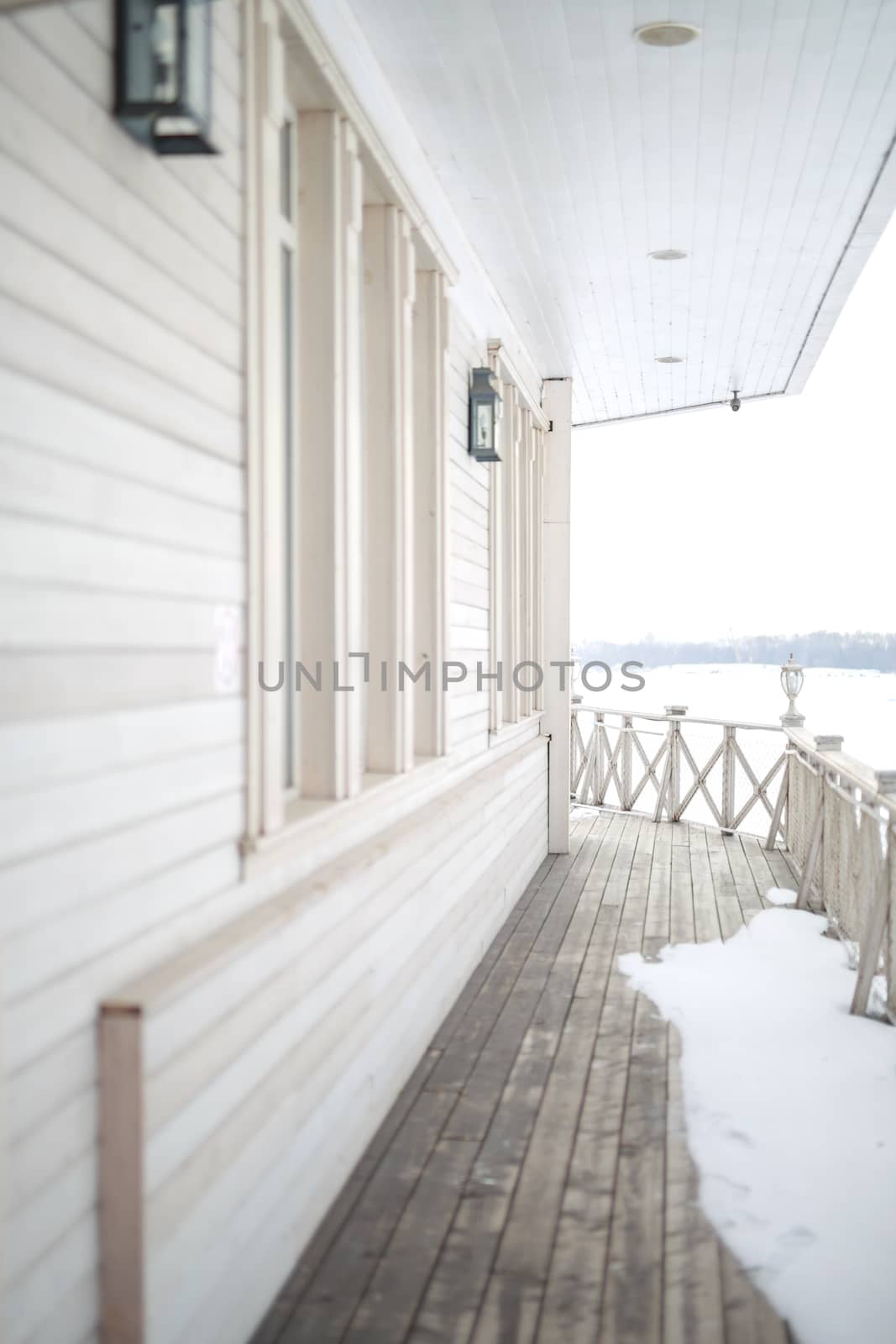 white snow on the wooden vintage open deck, old peeling paint light milk color, steel and copper lanterns hanging on the wall, snowy winter, snow lies on the river and the far shore of the earth is vi by dikkens