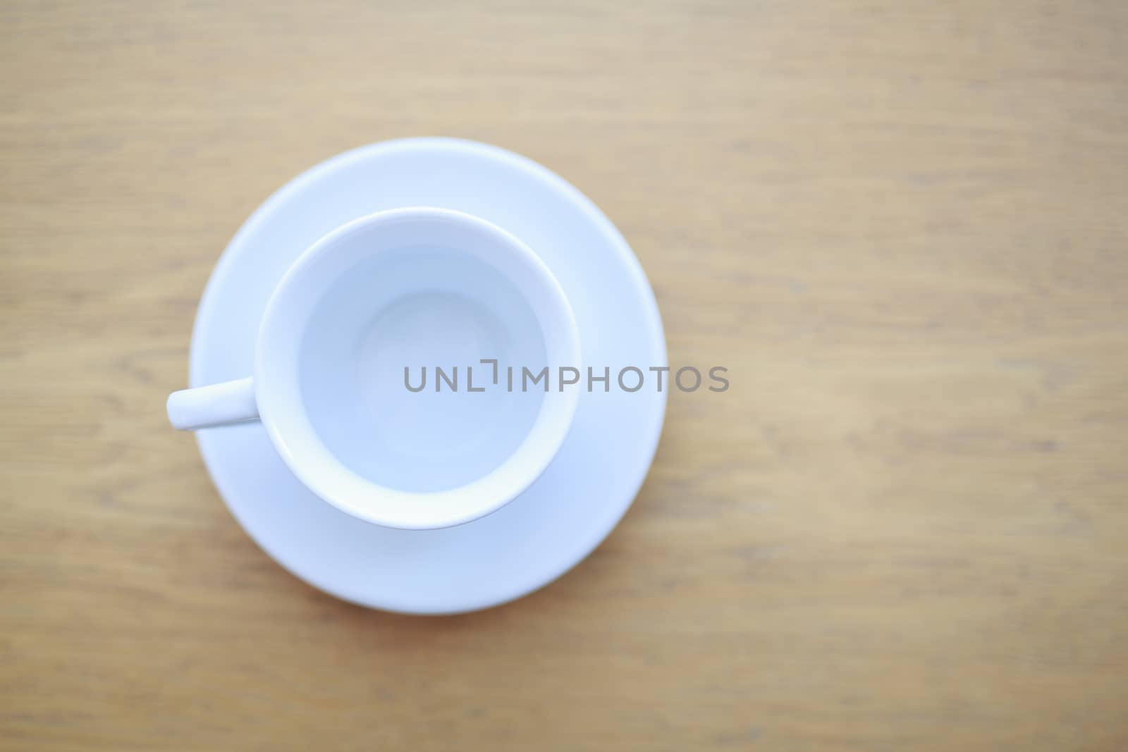 the view from the top one pure white ceramic Cup and saucer without drink sits on a wooden table in the afternoon sunlight