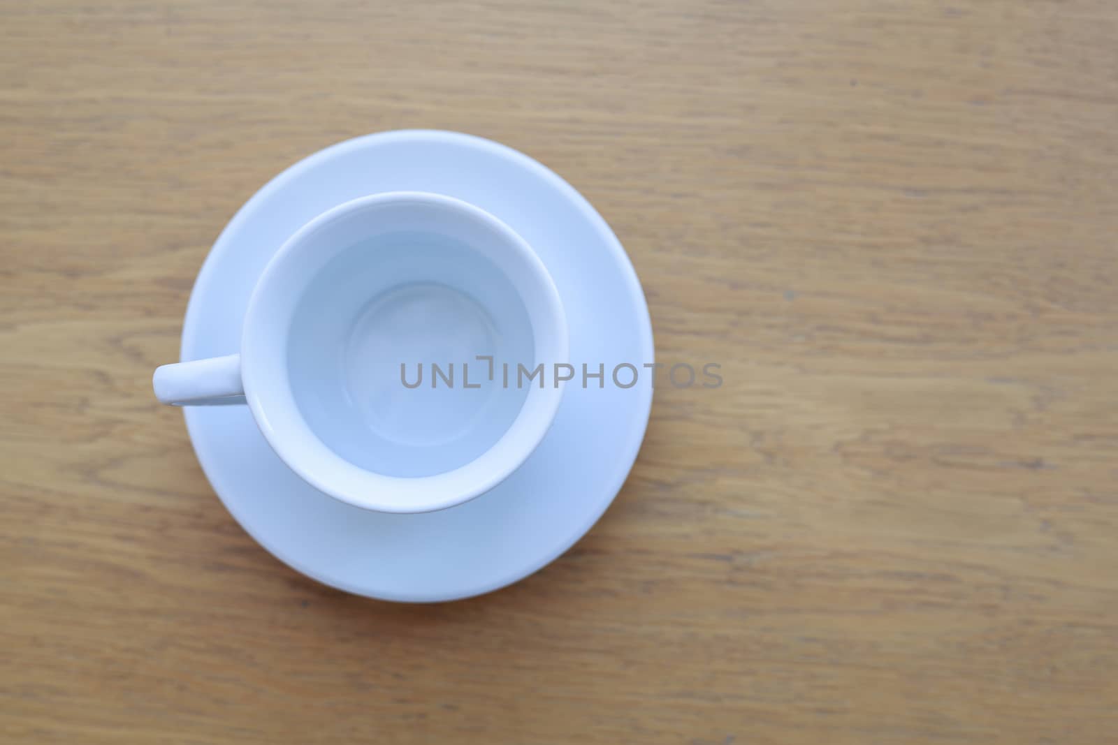 one pure white ceramic Cup and saucer without drink sits on a wooden table in the afternoon sunlight the view from the top