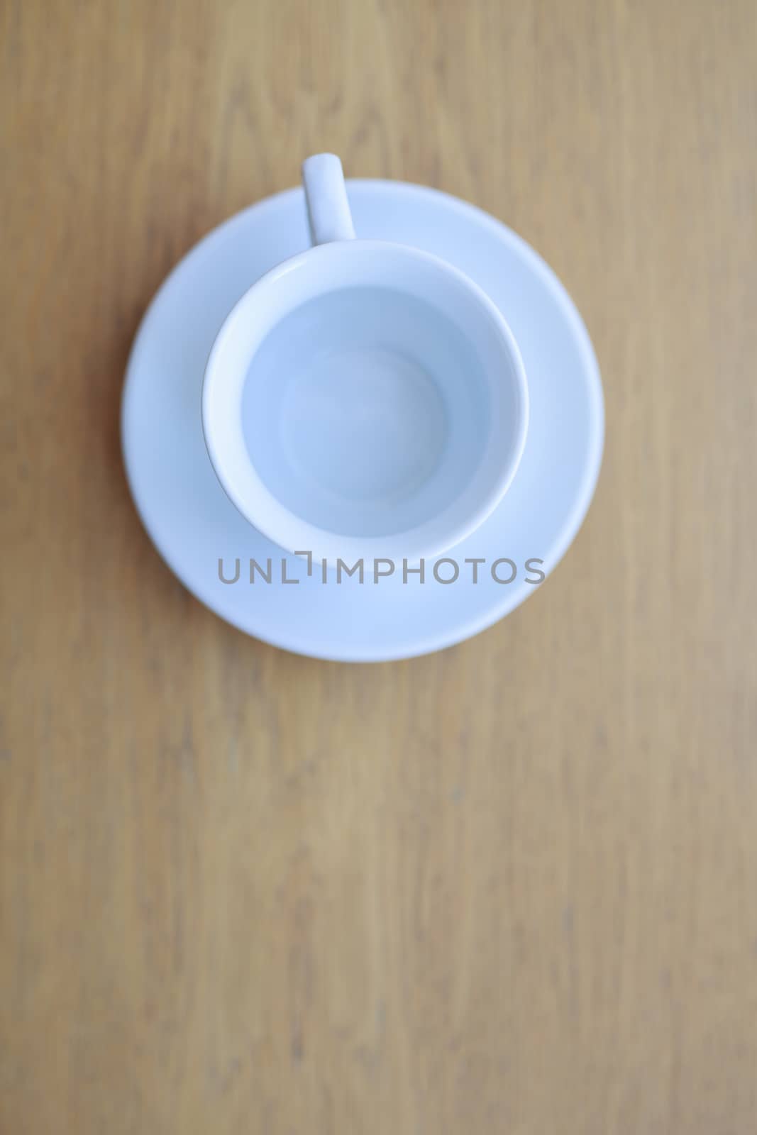 one pure white ceramic Cup and saucer without drink sits on a wooden table in the afternoon sunlight the view from the top