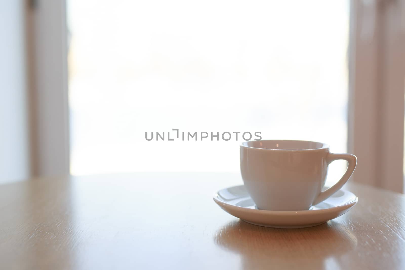 one pure white ceramic Cup and saucer without drink sits on a wooden table in the afternoon sunlight