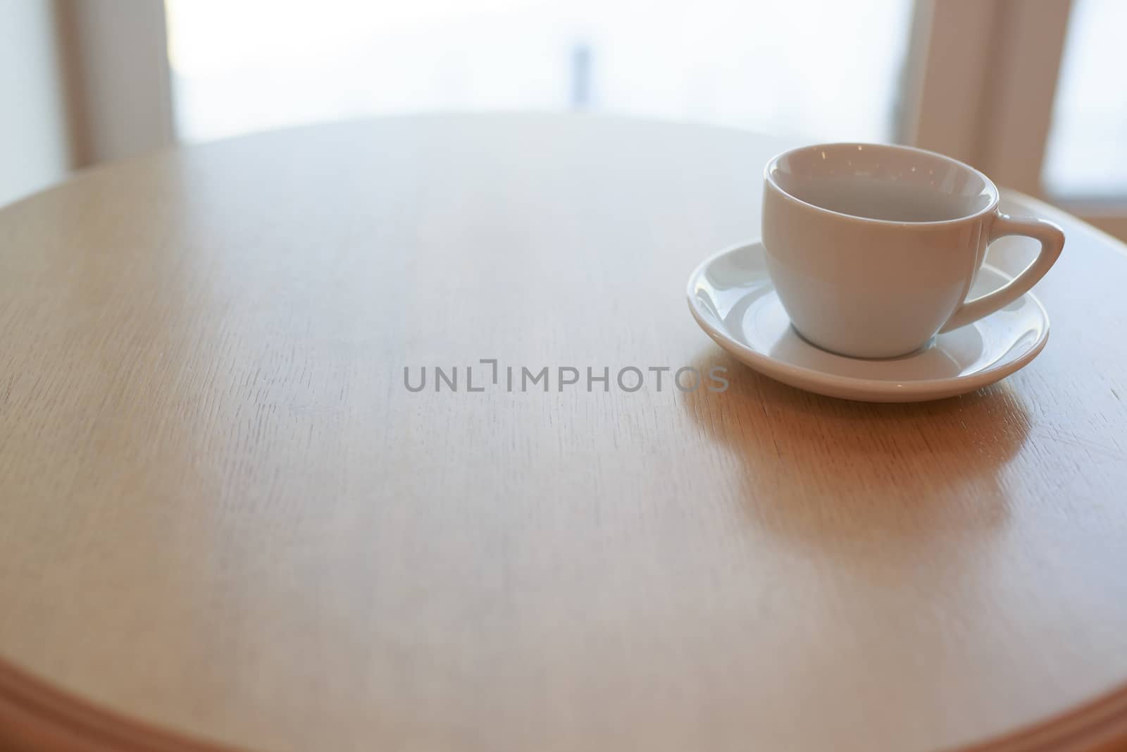 one pure white ceramic Cup and saucer without drink sits on a wooden table in the afternoon sunlight
