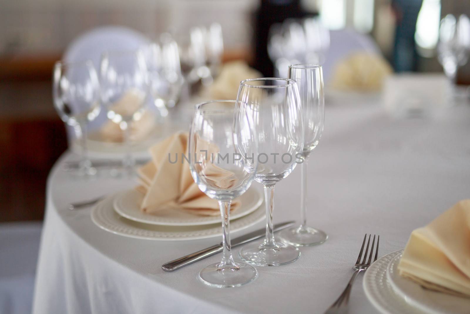 Cutlery on the table, clear glass champagne glasses, white tableware plate with beige peach napkin, knife and fork, table without people, clean tableware without food