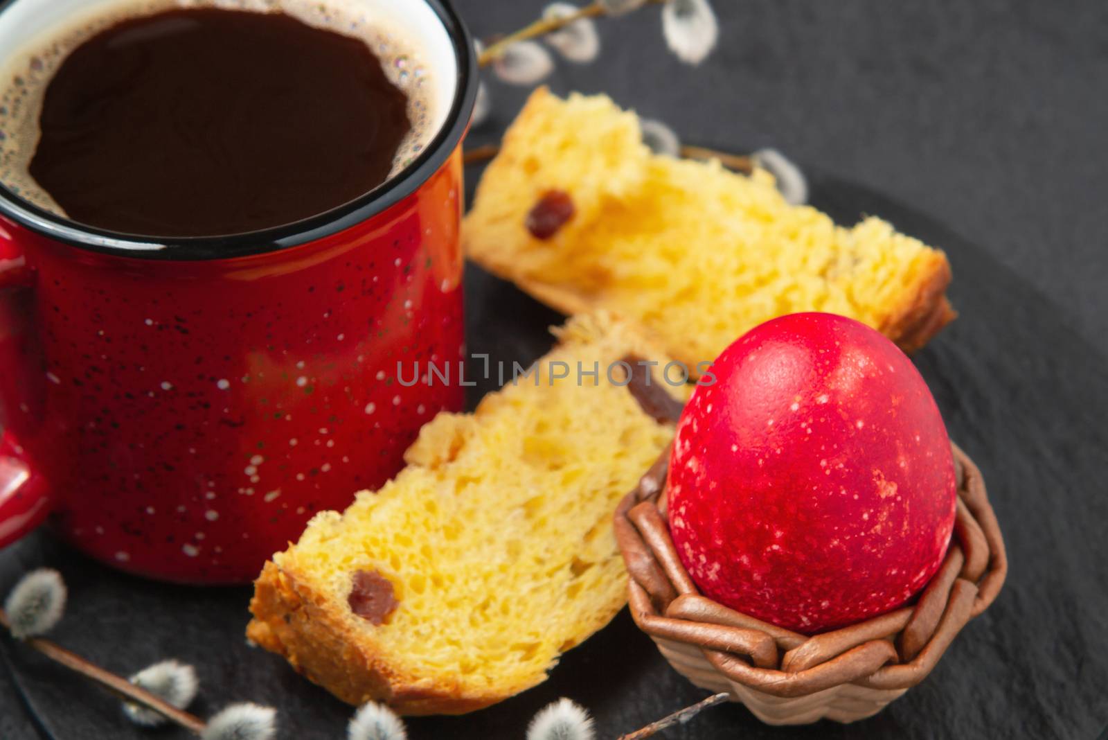 Red Easter egg, a slice of Easter cake and a cup of coffee on a cutting board on a dark table - traditional Easter breakfast