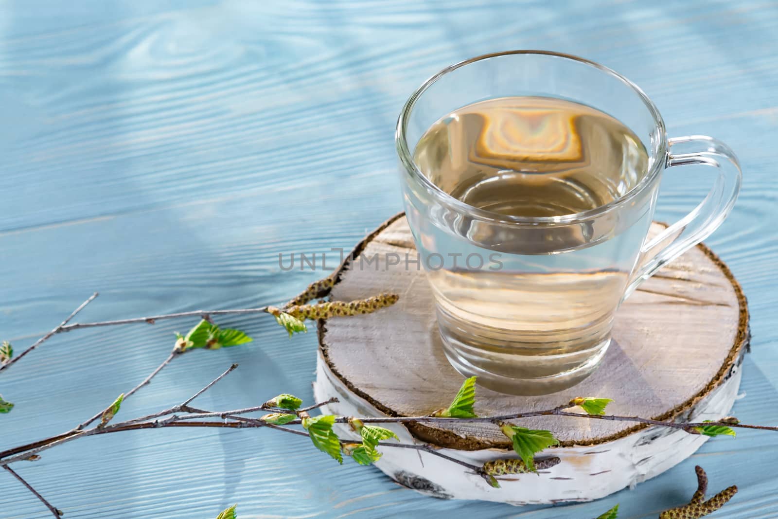 Birch juice on a blue wooden table in a glass mug, next to a branch of birch with young leaves, copy space, place for text.
