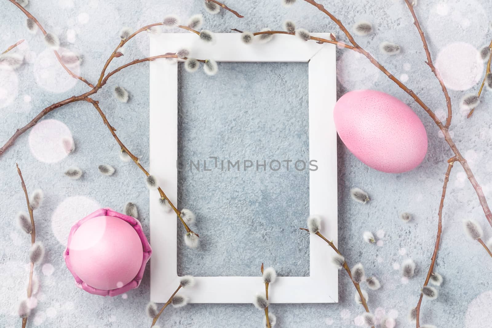 Pink easter eggs on gray table with willow twigs and white wooden frame - easter composition with copy space, flatlay by galsand