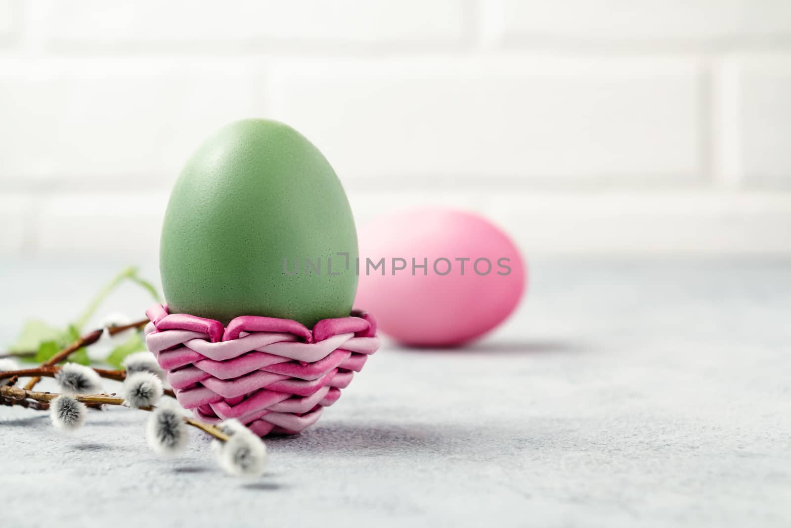 Pink and green Easter eggs in a wicker stand and on a gray table with pussy-willow twigs - Easter composition with copy space.