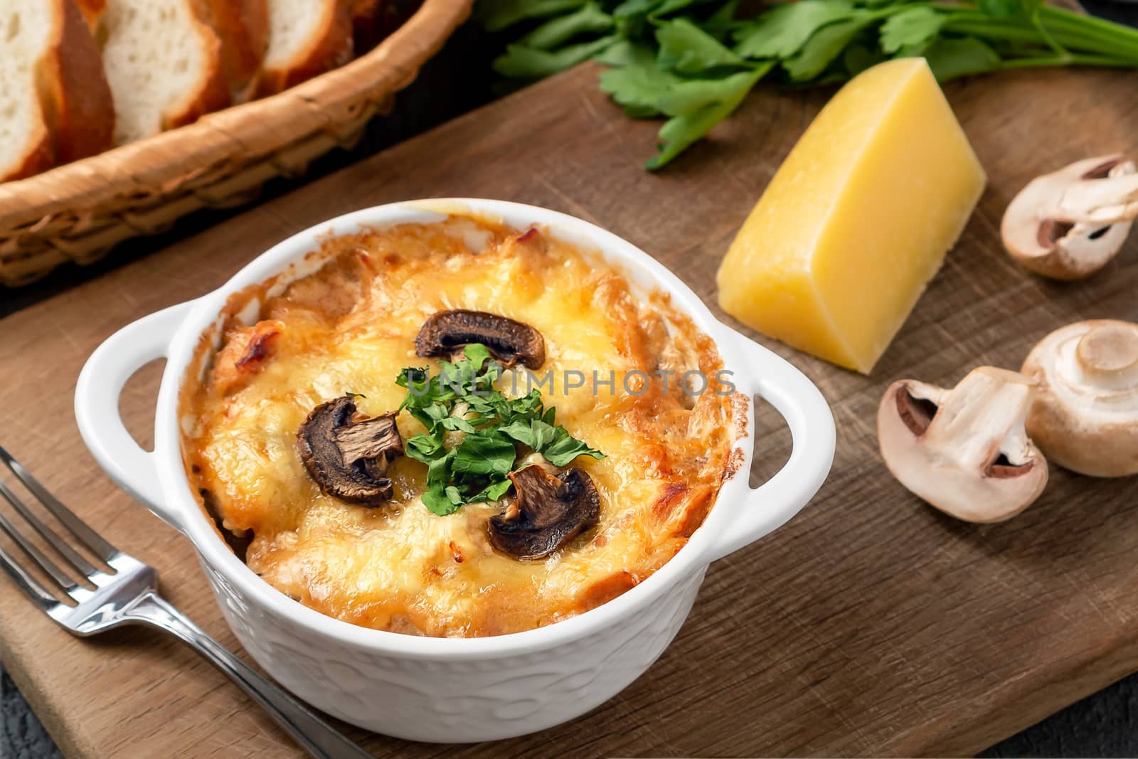 Casserole with chicken, mushrooms and cheese, known in Russia as julienne in white bowl with herbs on a wooden board, close up.