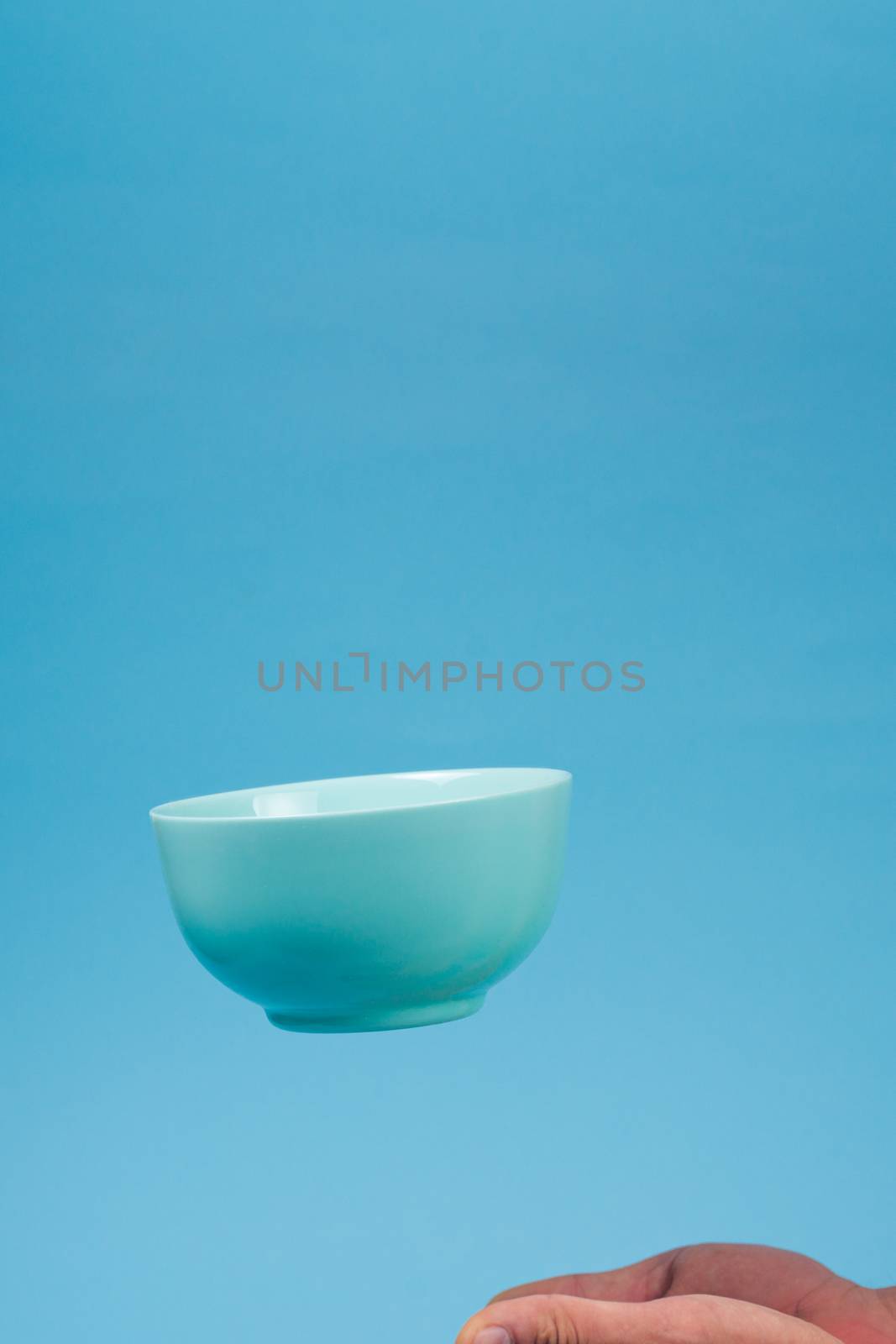 A blue ceramic mattle deep bowl for breakfast flying under male hands on blue background. Ideal photo for levitation of food and fruits or nuts.