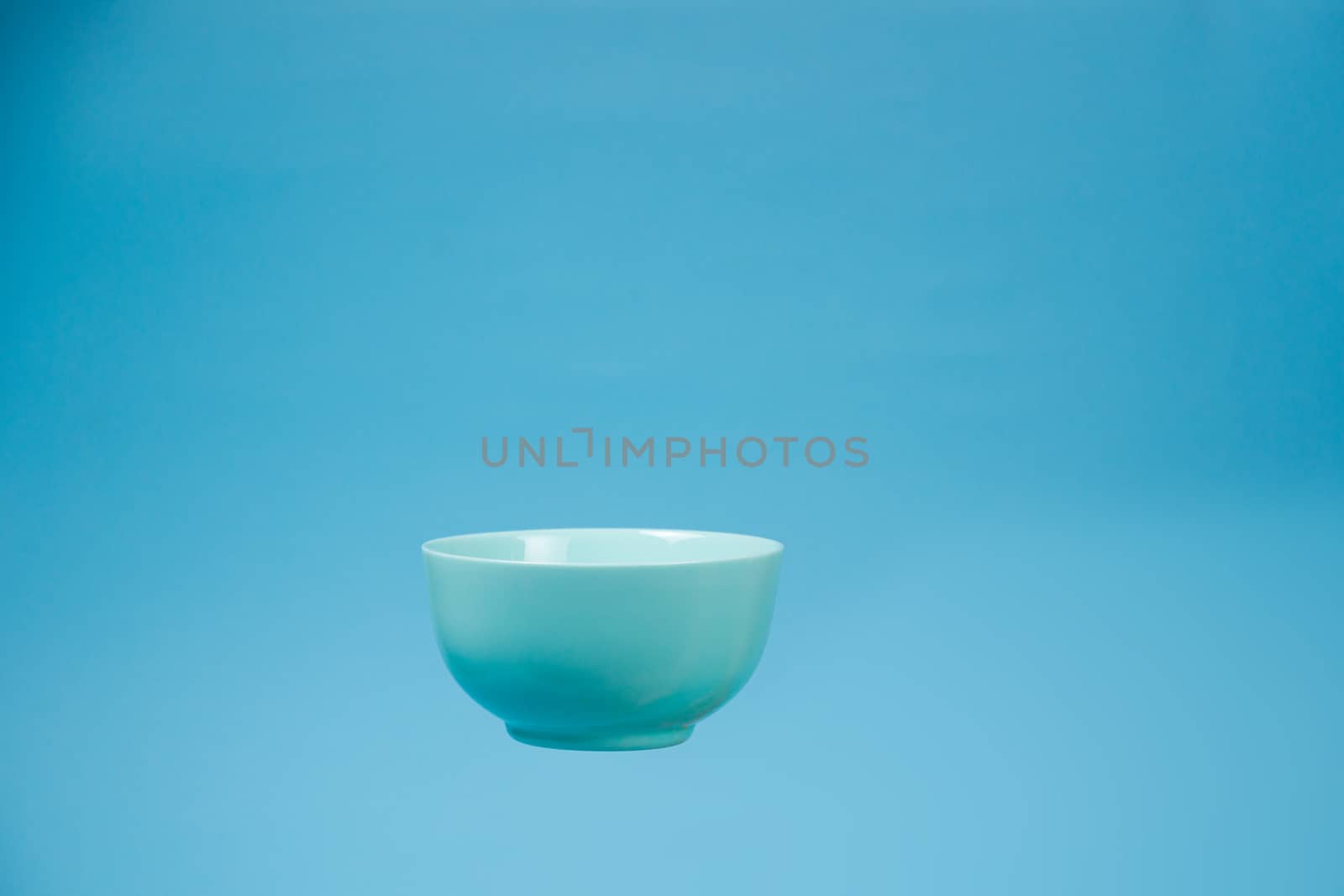 A blue ceramic mattle deep bowl for breakfast flying on blue background. Ideal photo for levitation of food and fruits or nuts.