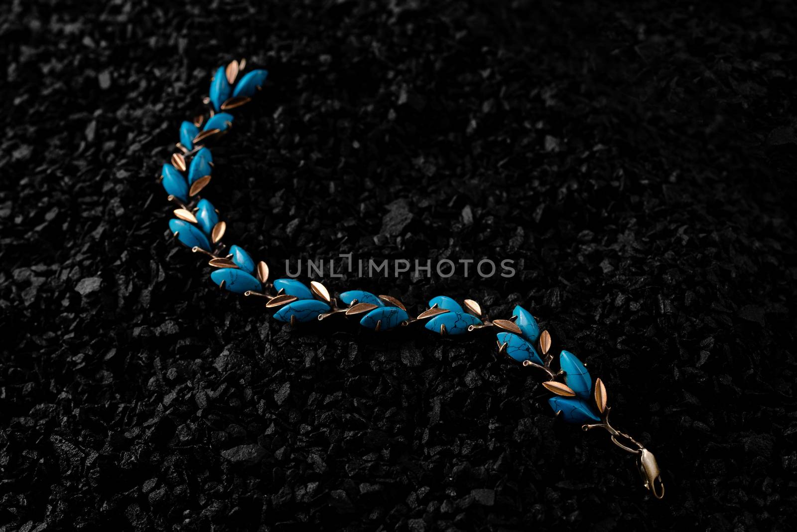 Unique handmade golden bracelet with turquoise inserts on a bunch of small black stones. Creative photo of unique jewellery.