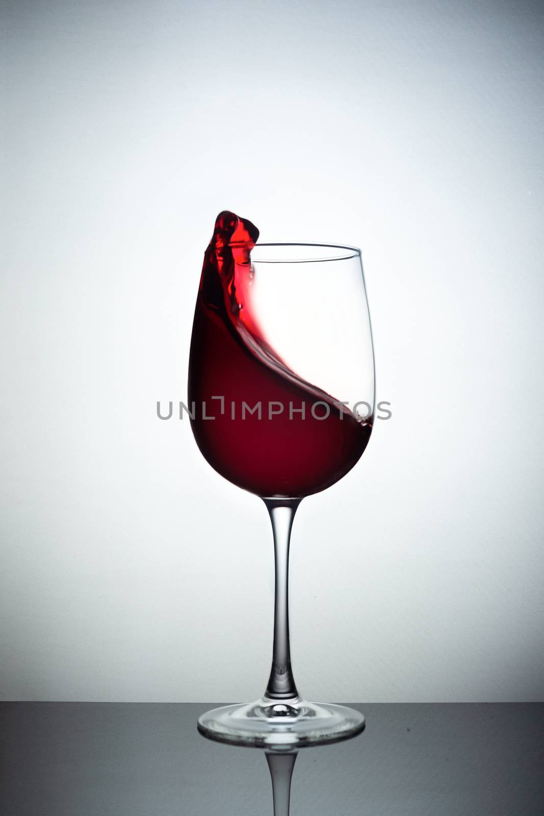 Creative photo of wine glass with storm in a glass on white background. A wine glass filled wine and a wave of wine flies from a wine glass. Wine glass stay on black glass sheet. Stock liquid motion photo.