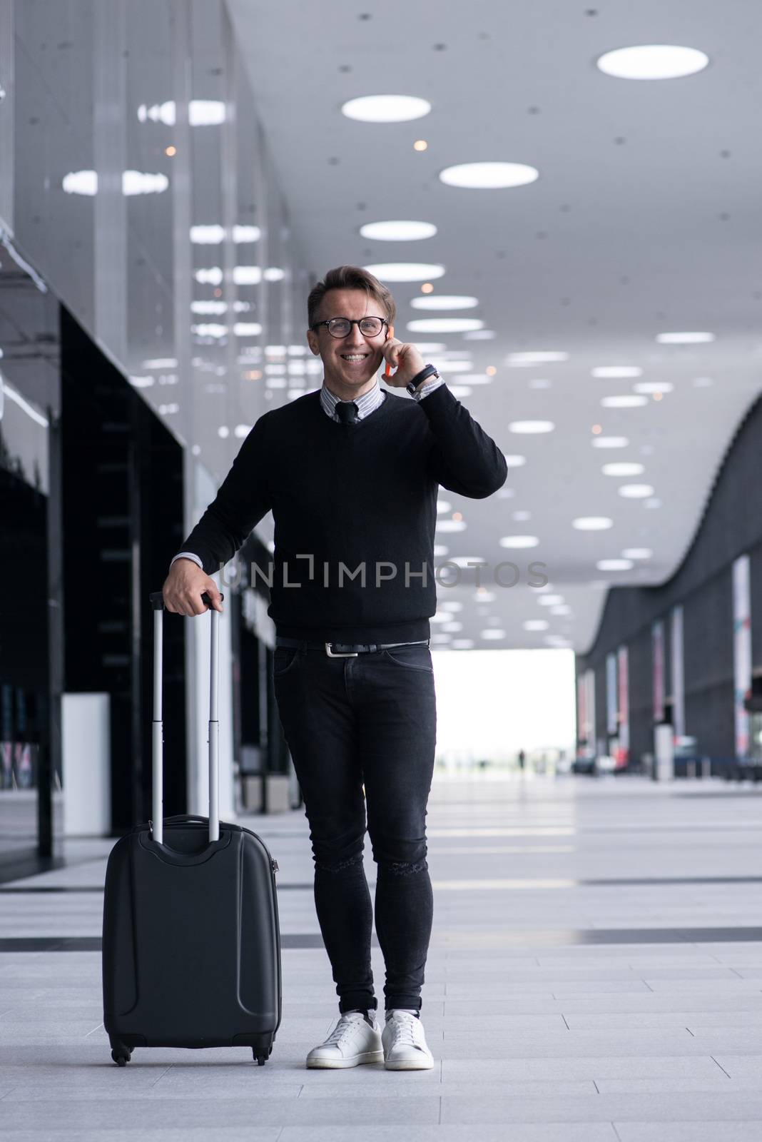 Man walking with wheeled bag at airport terminal and talking on phone