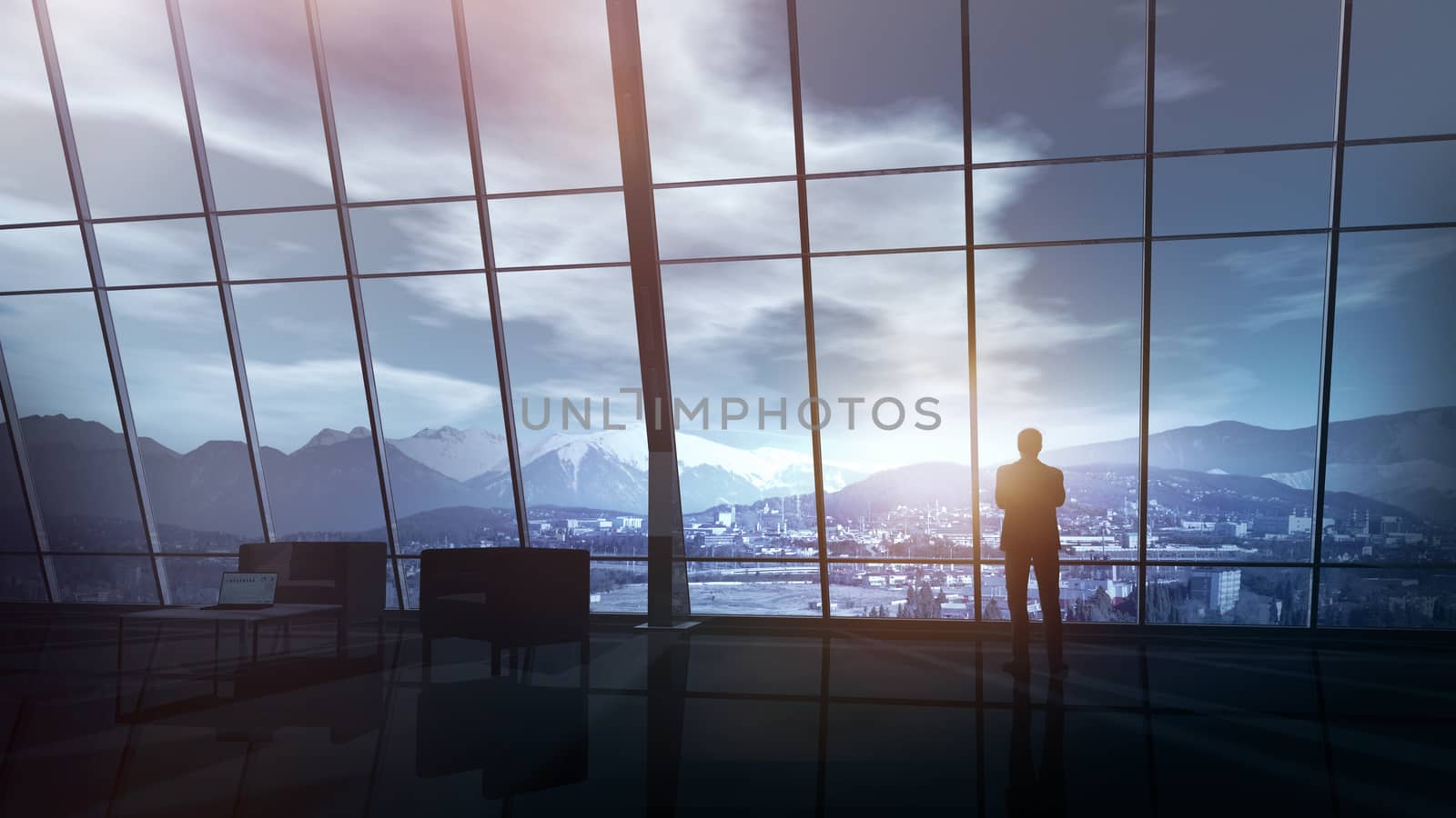A businessman in his office looks through a large panoramic window overlooking the snow-capped peaks of the mountains.