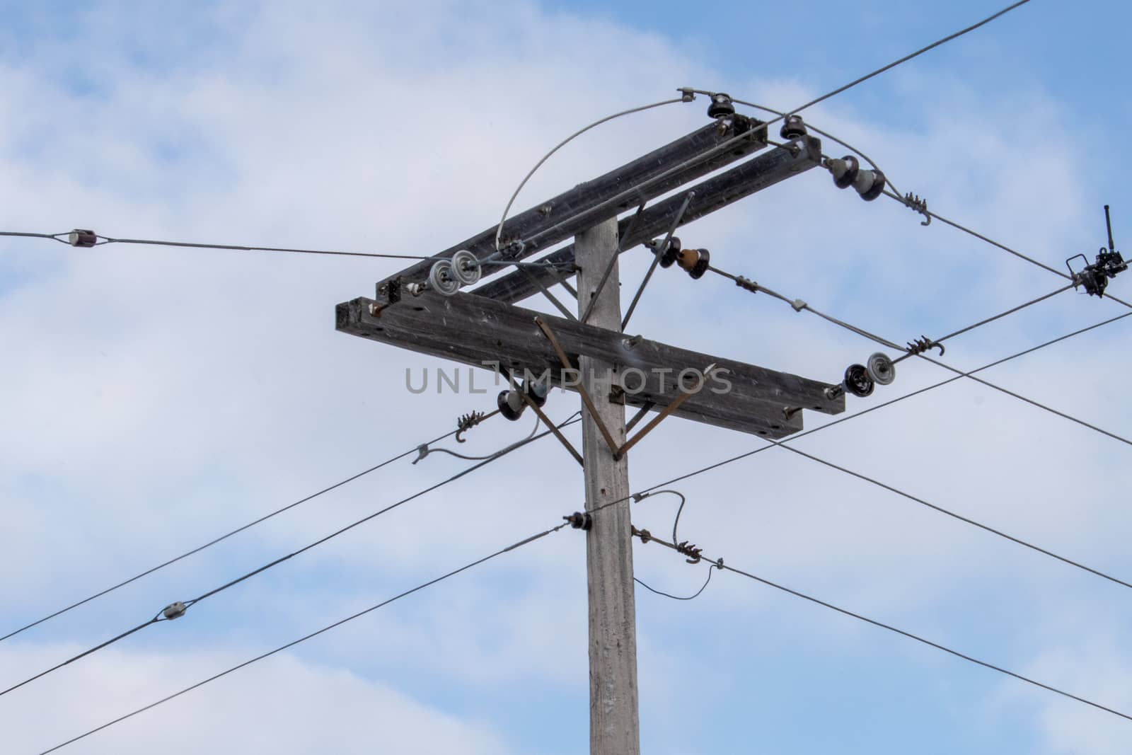 A rural junction of electrical wires is elevated by a wooden pole. The connections of power lines transmit electricity in all directions, carrying them to nearby homes and towns.