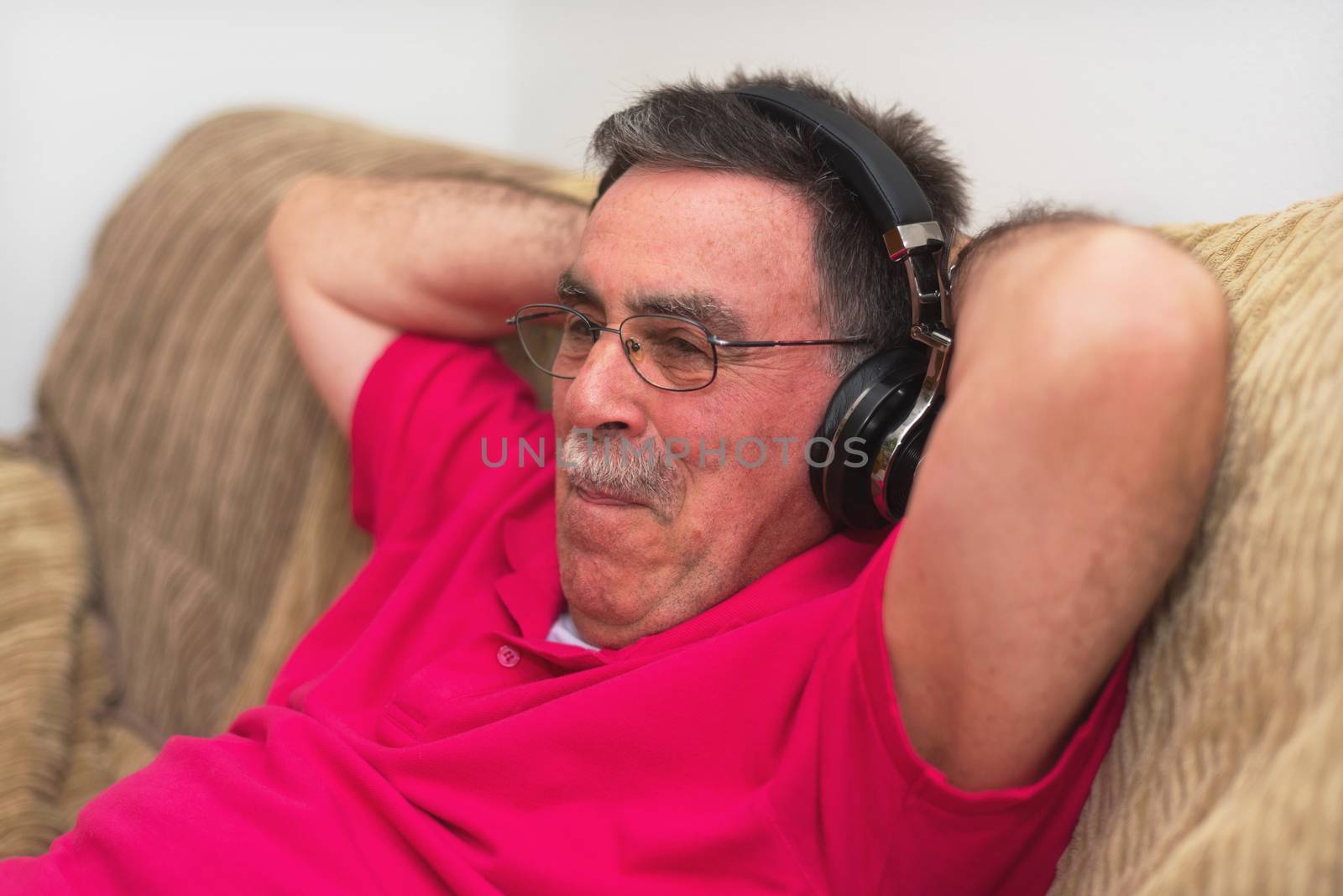 Relaxed Senior man in headphones listening to music at home by HERRAEZ