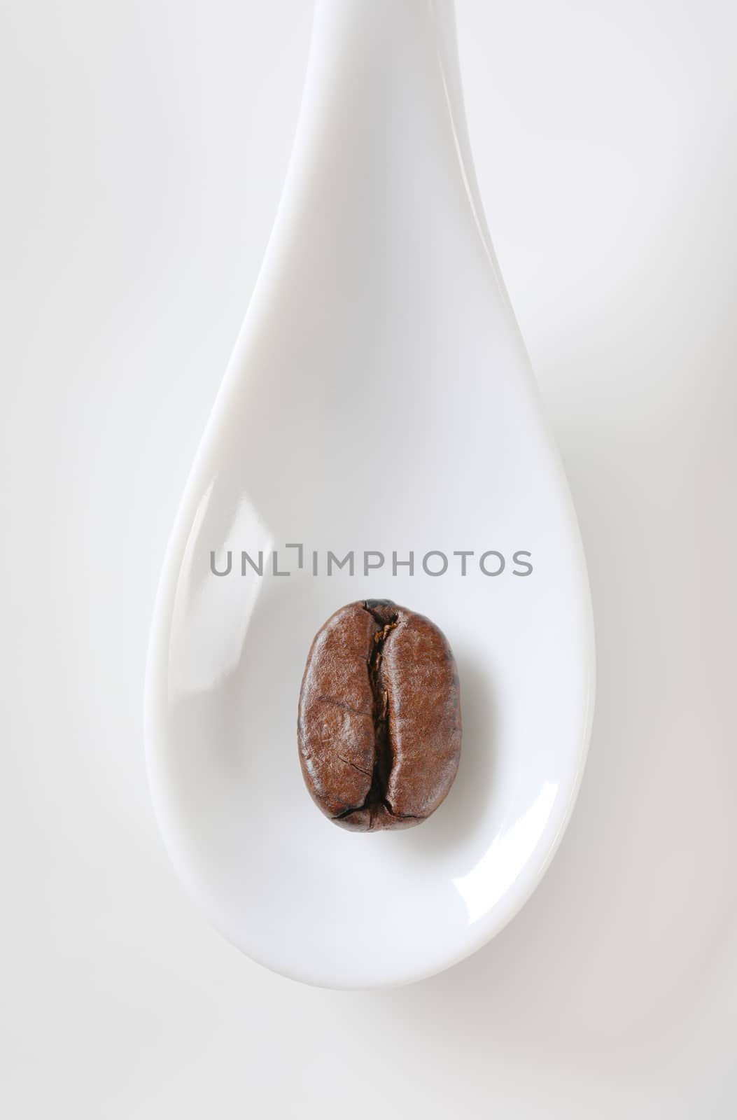 Single coffee bean on white spoon by Digifoodstock